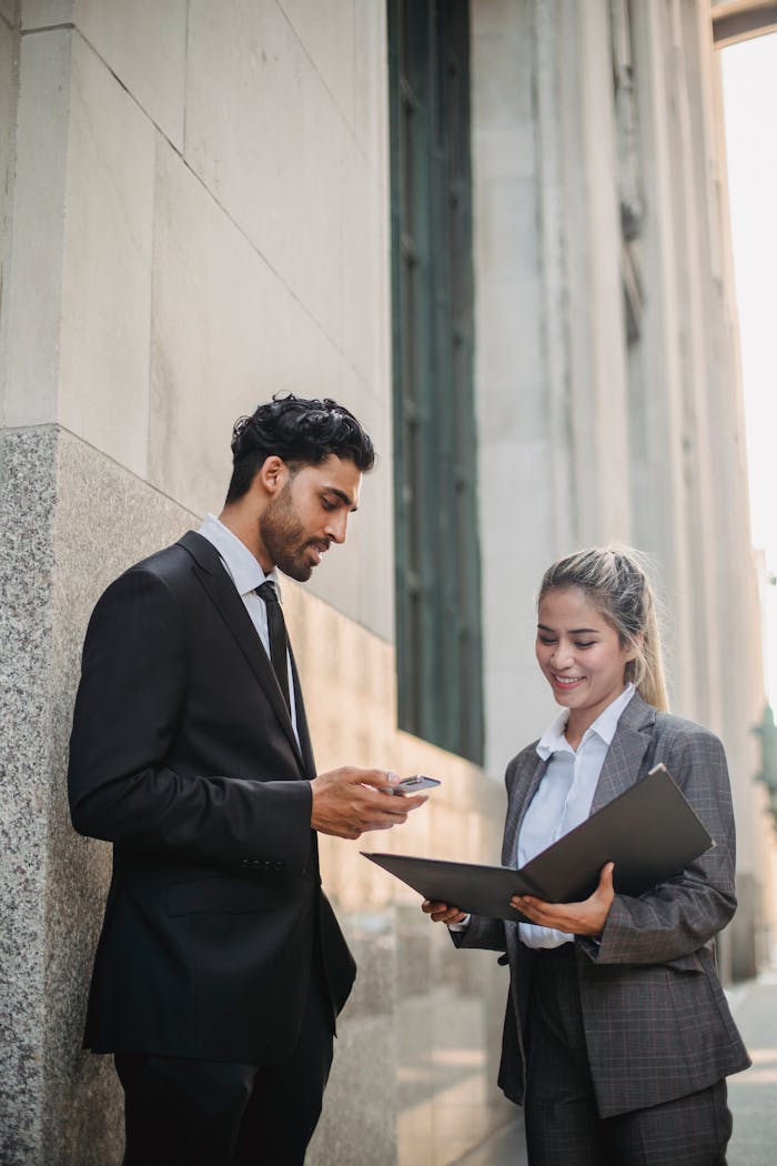 Two professionals in formal attire discuss documents outdoors, showcasing confidence and partnership.