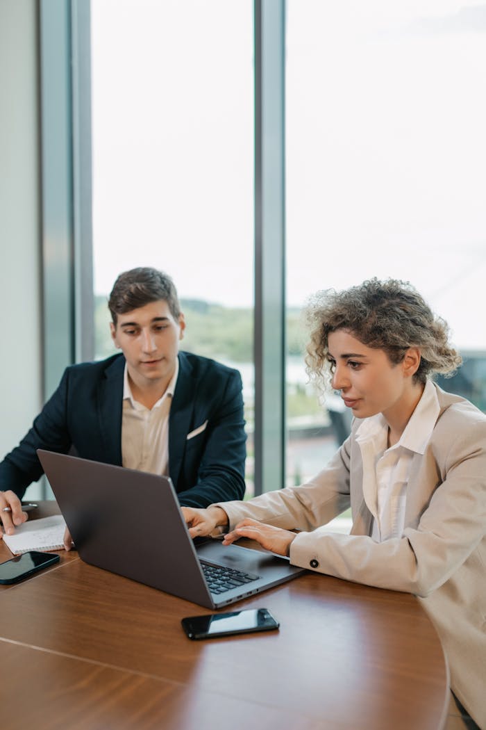 Colleagues in business attire working together on a laptop in a modern office setting.