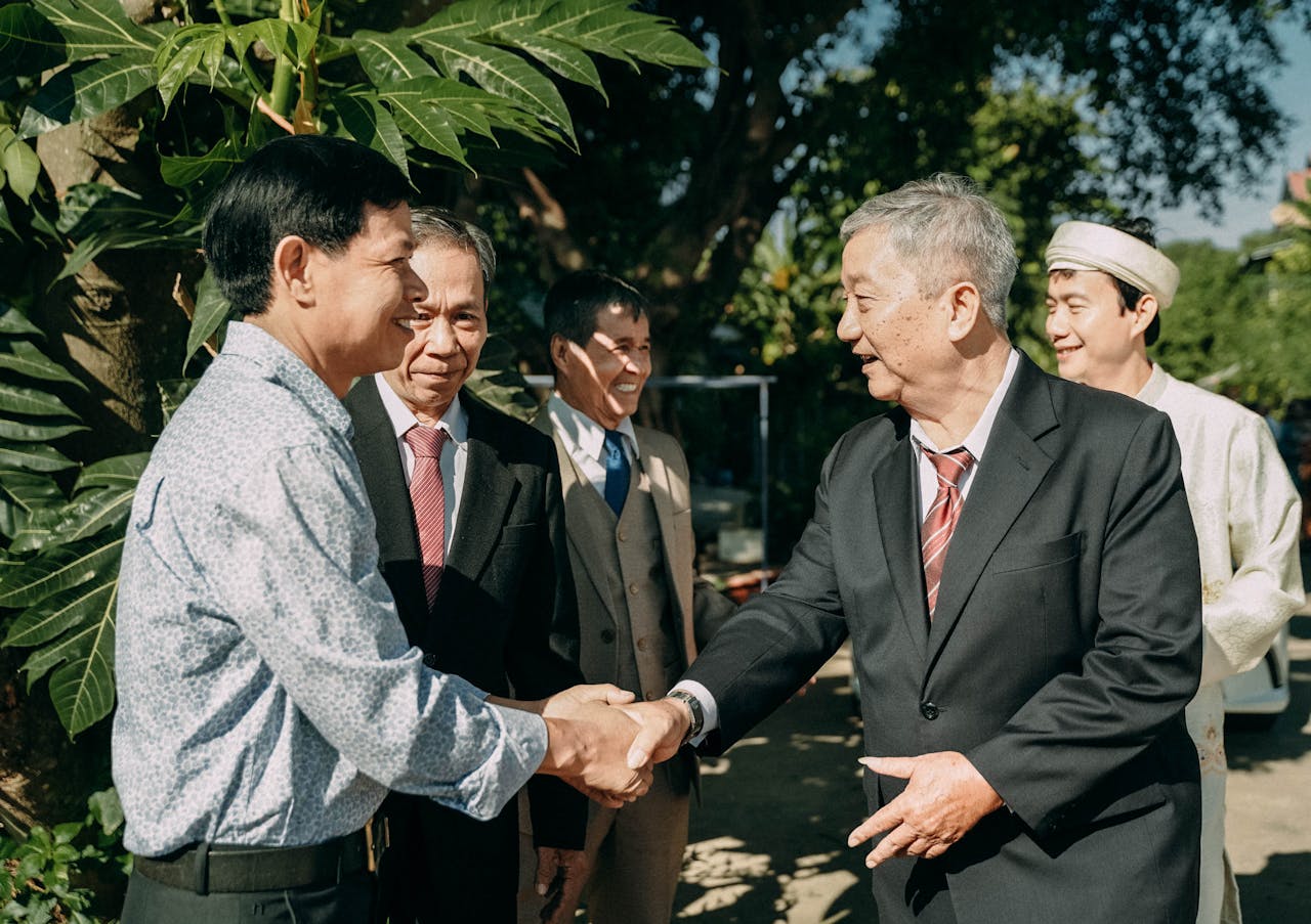 A group of businessmen in formal attire exchanging handshakes in an outdoor setting.
